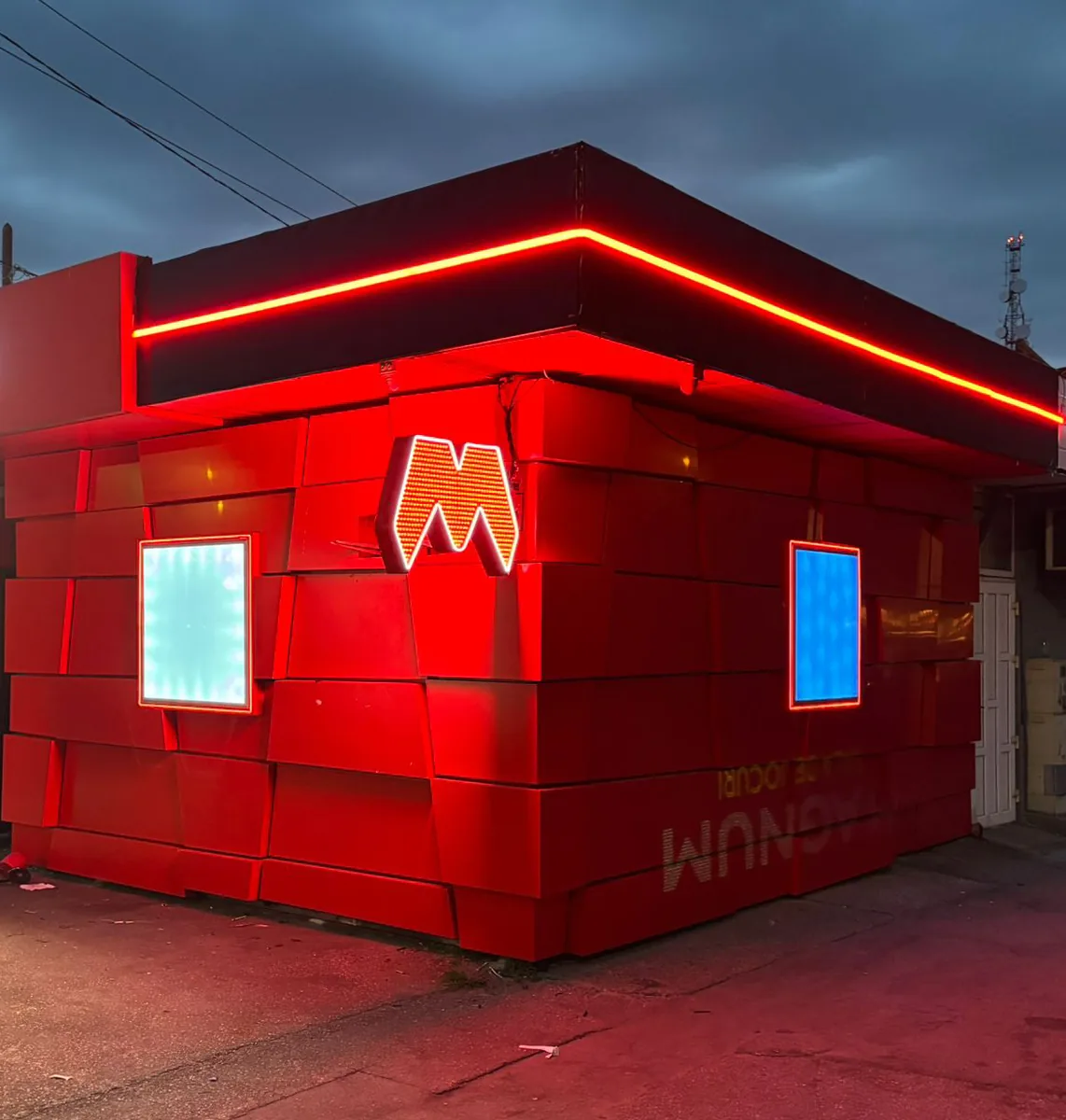 Chioșc comercial cu fațadă roșie și firmă tip neon, fotografiat noaptea — Lartek Grup