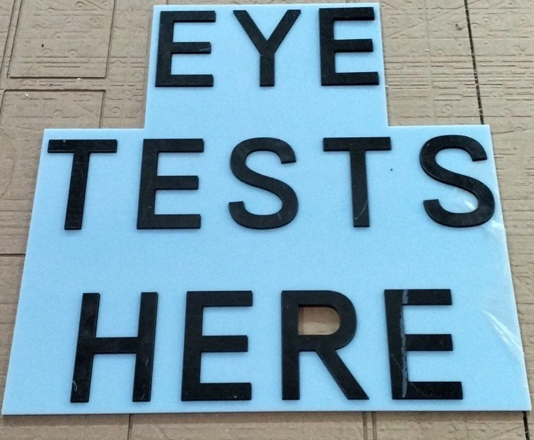 Panou cu textul EYE TESTS HERE, din litere negre decupate pe CNC aplicate pe placă albastru deschis — Lartek Grup